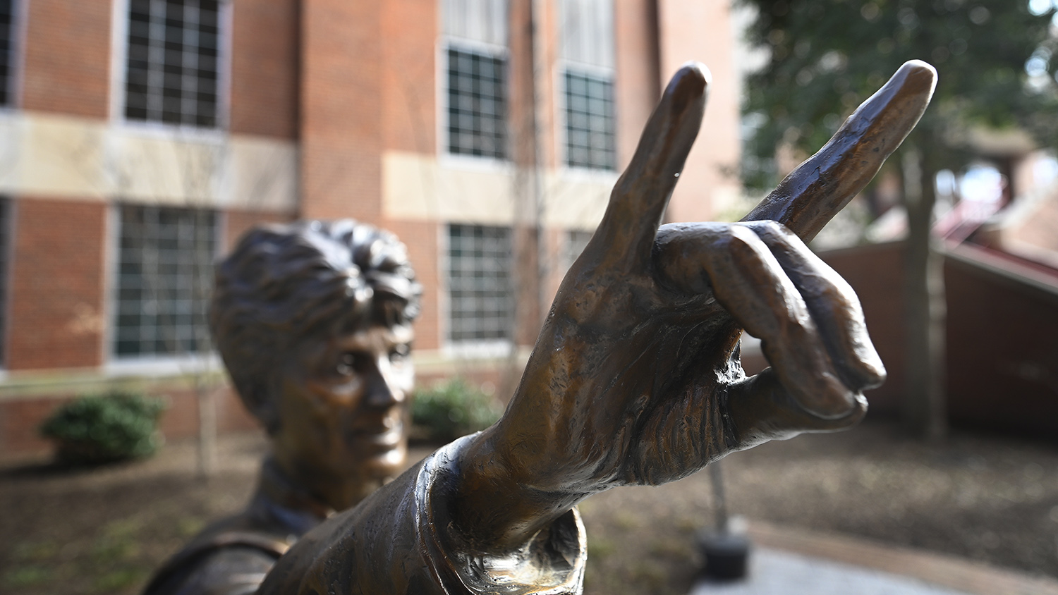 up close photo of statue of former NC State Wolfpack women's coach Kay Yow with hand in classic "wolf" gesture