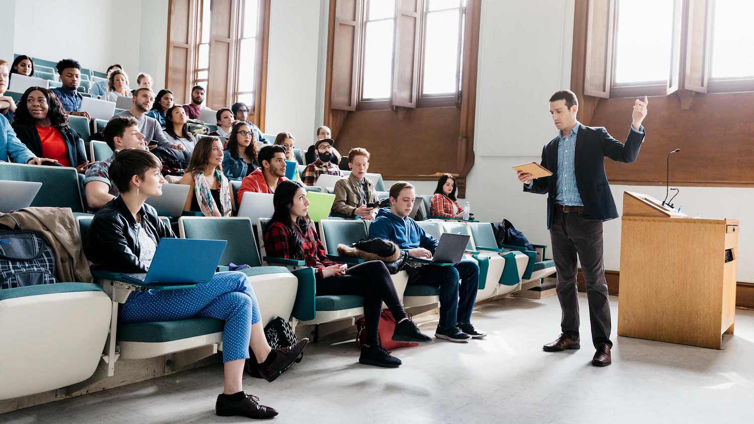 An instructor using Top Hat in his course. He is standing at front of large classroom using a Tablet. Students have cellphones in hand.