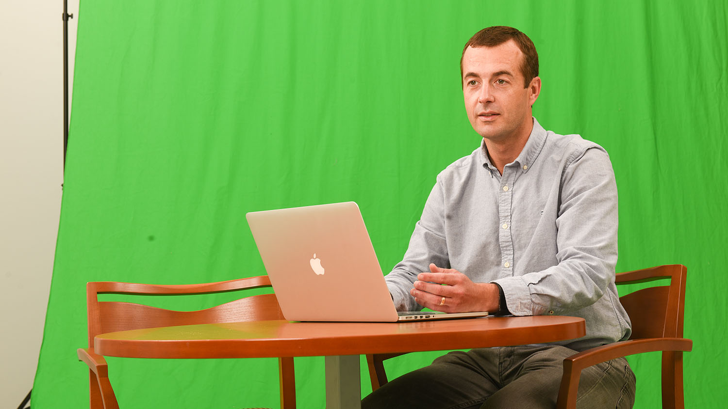 Clint Stevenson sitting at a table with a laptop in front of a green screen.