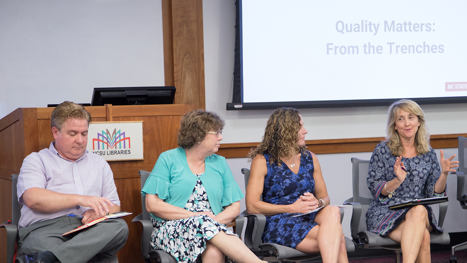 Members of the first cohort of the Online Course Improvement Program facilitated a panel discussion at Summer Shorts 2018. Pictured left to right: Paul Mulvey, Cheryl Block, Amanda Edwards and Tracy Appling. Not pictured: Marne Coit, Ana Gray and Jill Grifenhagen. The group sits in front of the audience. Tracy Appling is speaking and the other OCIP members are looking at her.