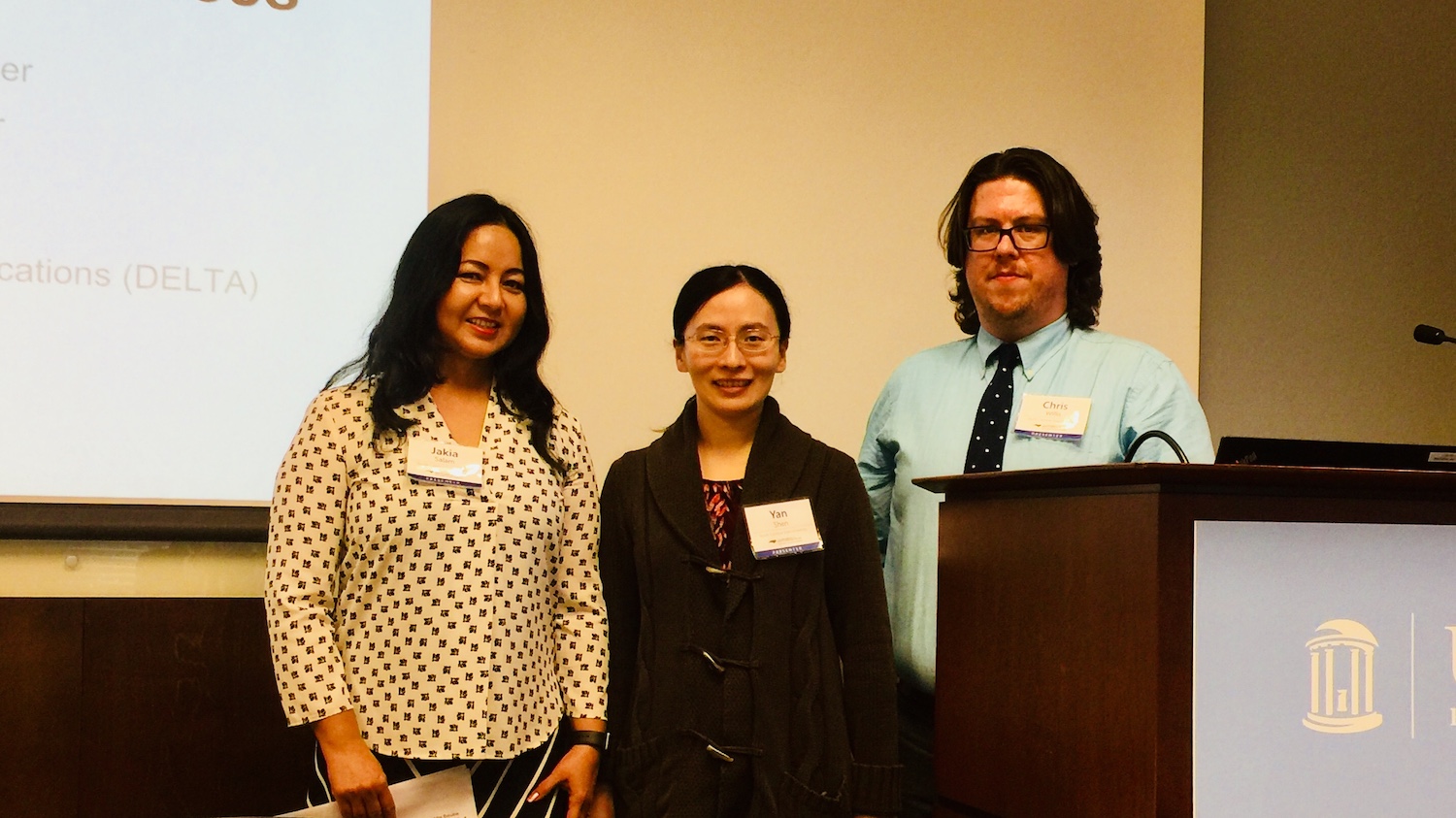 DELTA Staff members (left to right) Jakia Salam, Yan Shen and Chris Willis at the 2019 UNC System Student Success Conference. The group is standing in front of a screen and behind a podium at the conference.