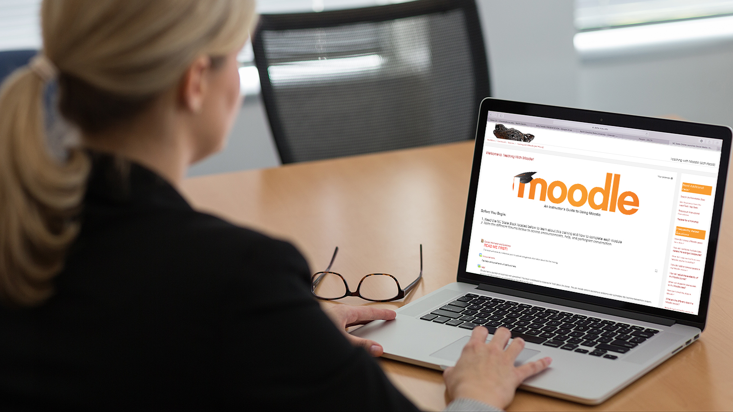 Decorative: Woman working on laptop that displays Moodle logo.