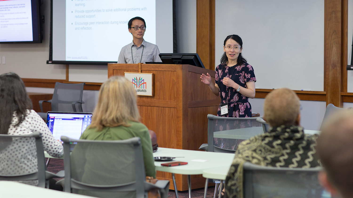 Instructional Designer Yan Shen (right) gives a presentation at the 2018 Summer Shorts. Yan is pictured at the front of the room with participants in the crowd.