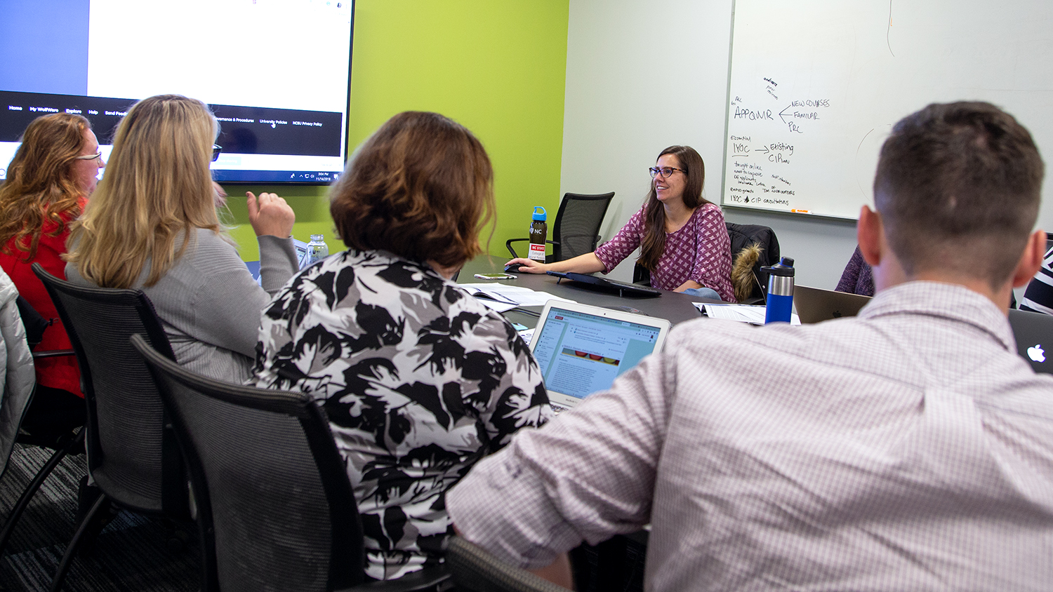 Instructional Designer Bethanne Tobey (center) facilitates a face-to-face working meeting of the Fall 2018 Online Course Improvement Program cohort. Bethanne is pictured at the back of the table with participants on the other side.