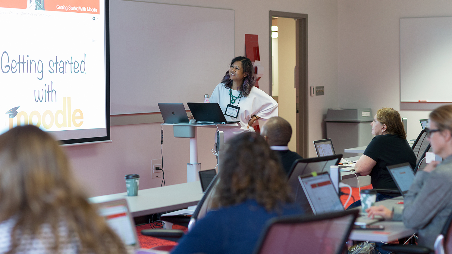 Instructional Technologist Arlene Mendoza-Moran leads a session about Moodle at the 2018 Summer Shorts in Instructional Technologies program. Arlene is at the front of a classroom looking at a screen that says "Getting Started with Moodle" participants are sitting at tables and also looking at the screen