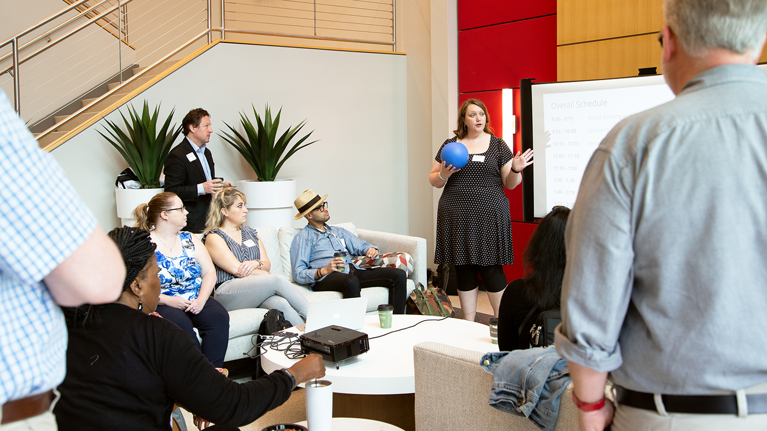 Bethany Smith stands in the middle of a group holding a blue microphone ball. Attendees sit and stand around listening to her. Photo is in the CTI lobby.