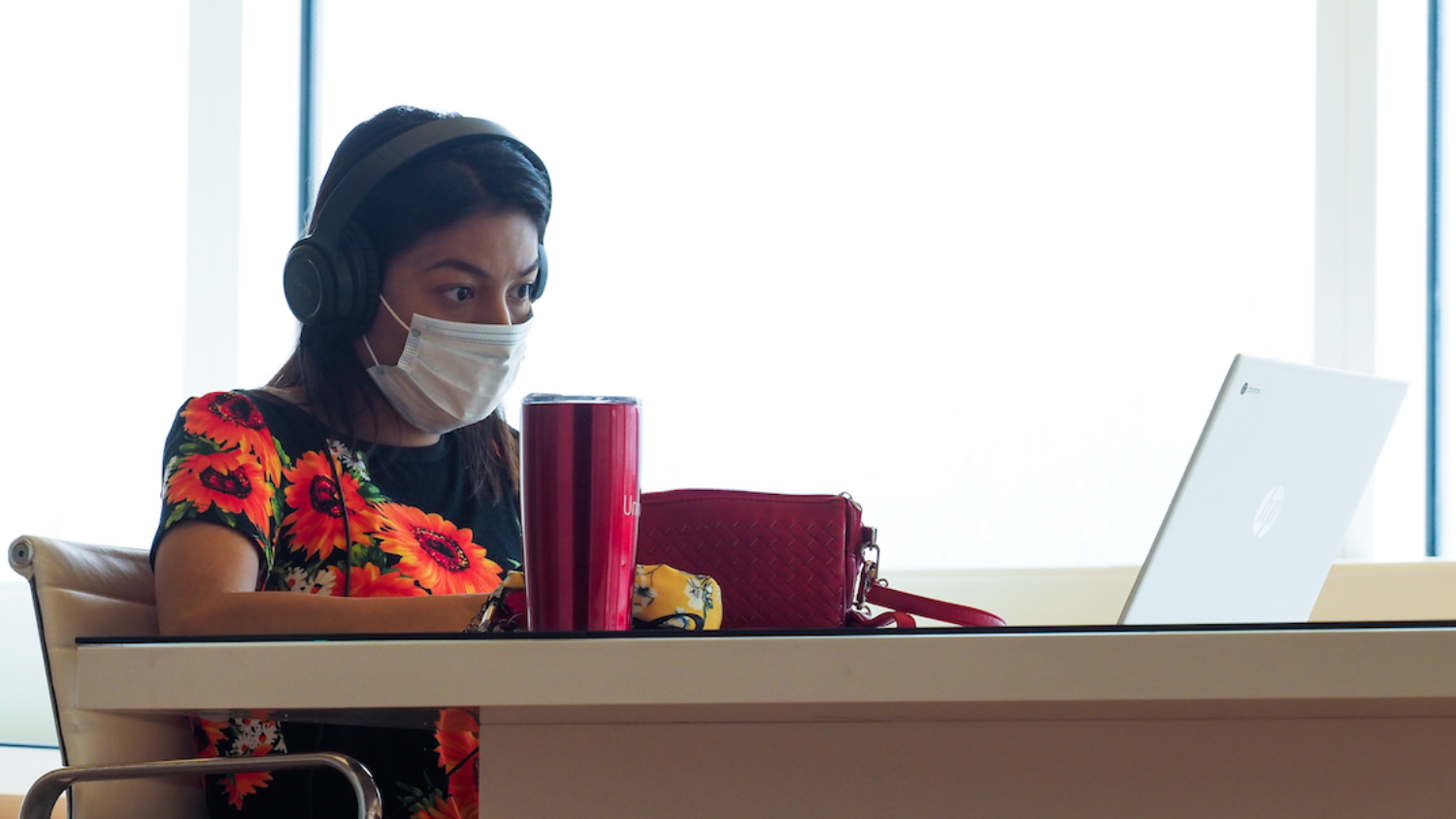 Person sits at a table with mask, headphones and a laptop