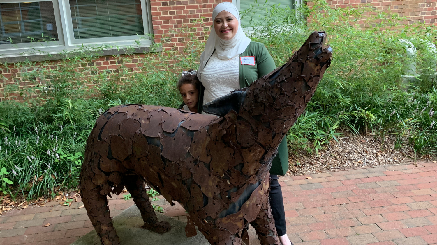 Gadeer and a child pose with a metal wolf statue outside of Nelson Hall.