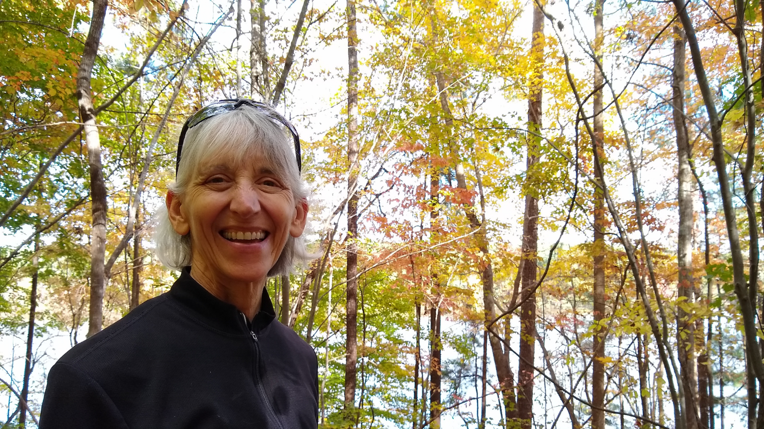 Annette Moore smiles in front of woods and a lake view.