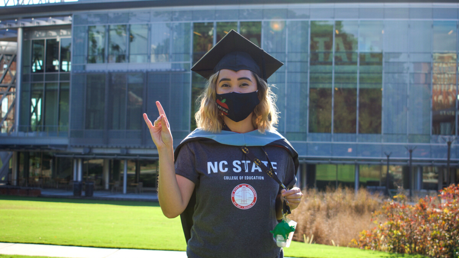 Student poses for photo in a graduation cap and mask in front of Talley Student Union