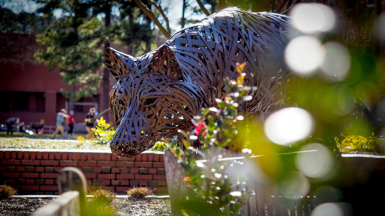 Students enjoy outdoor time on a warm spring day in the background of one of the copper wolves at Wolf Plaza.