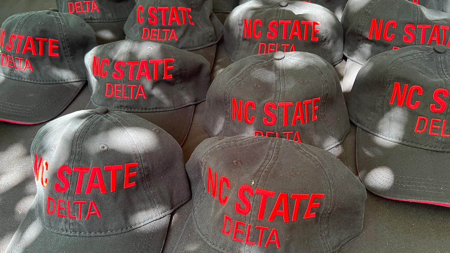NC State DELTA ball caps on a table