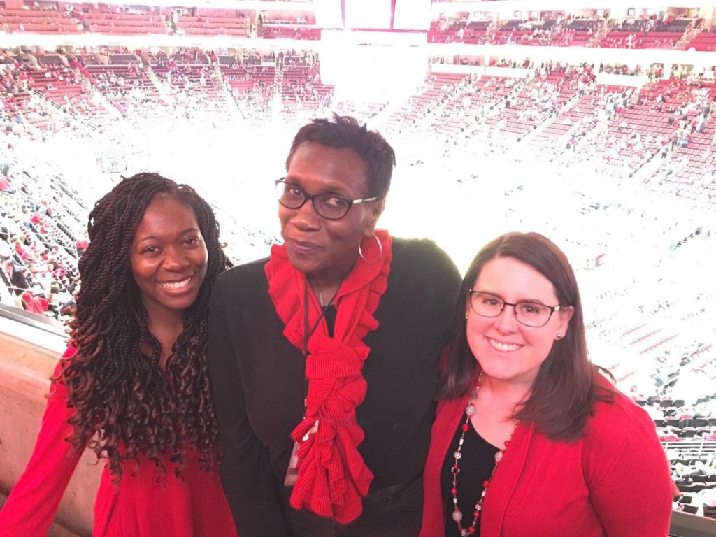 Jessica White standing with NC State colleagues in a crowded basketball stadium