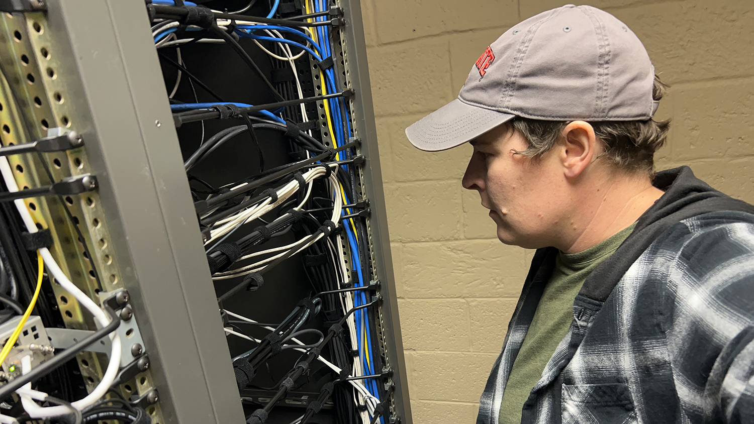 Networking Technician Jess Benton shown looking at cables as she checks the signal flow for DELTA lecture capture equipment.