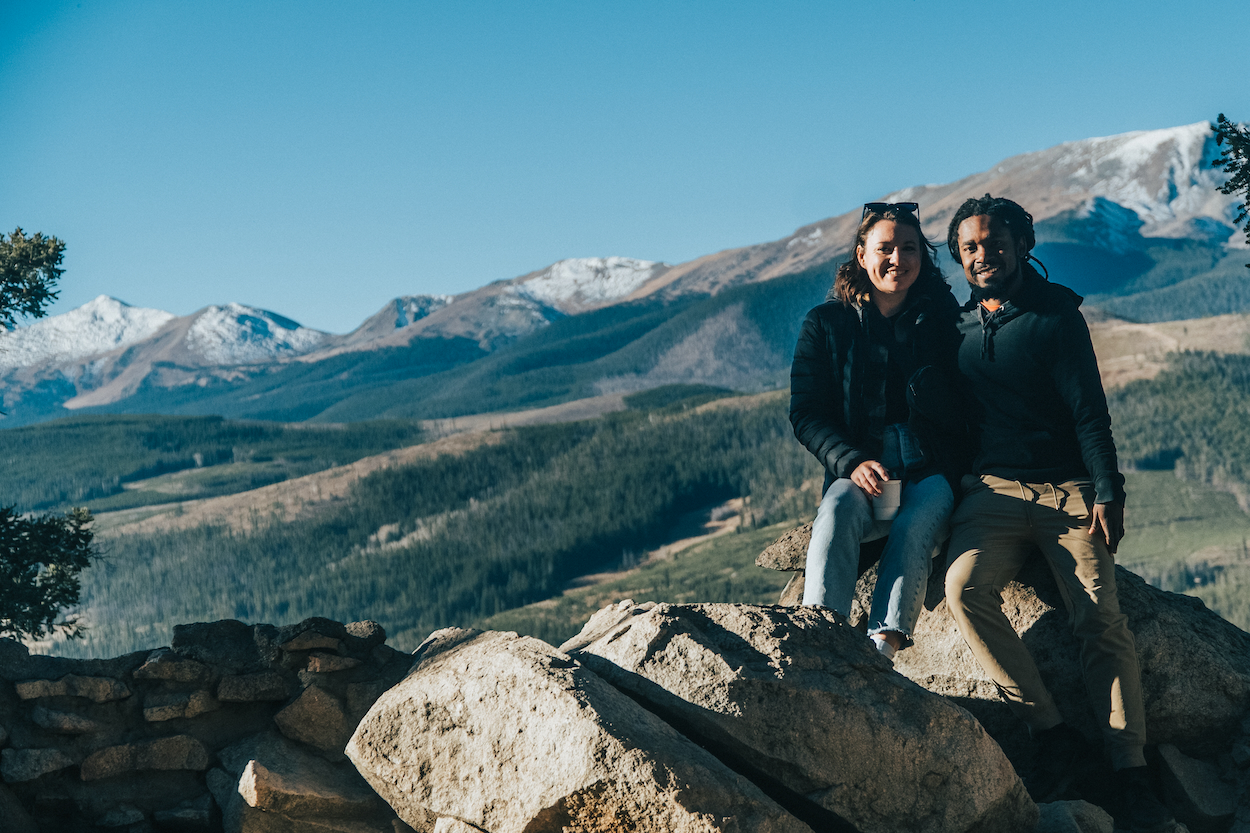 Relly Moorer with his wife, Abigail, sitting on a rock with a mountain vista in the backgroun at Sapphire Point Overlook in White River National Forest, Colorado