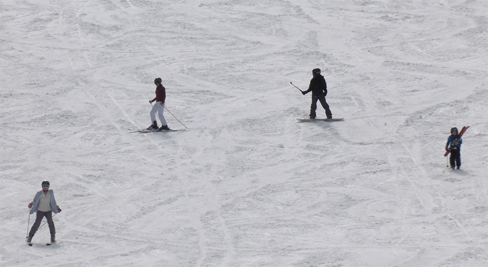 Snowboarders and skiers shown on a snowy hillside being recorded by Relly Moorer using a camera