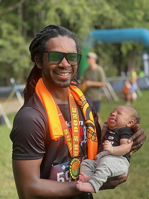 Relly Moorer wearing his finisher's medals and holding his infant son after completing a half marathon race