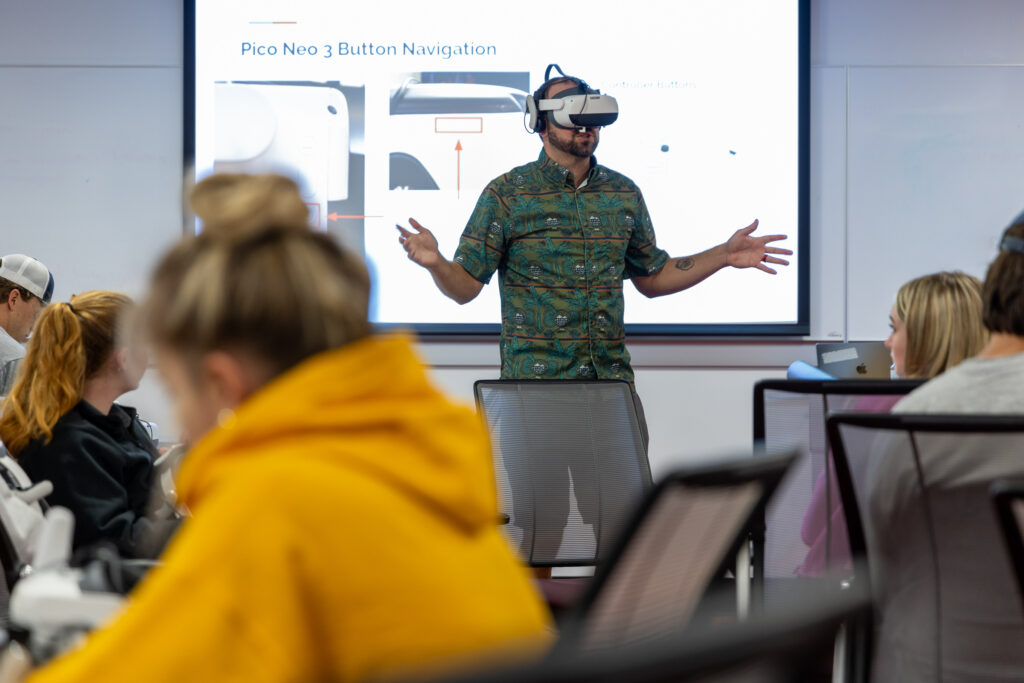 A man in front of a classroom of students wearing a virtual reality headset.
