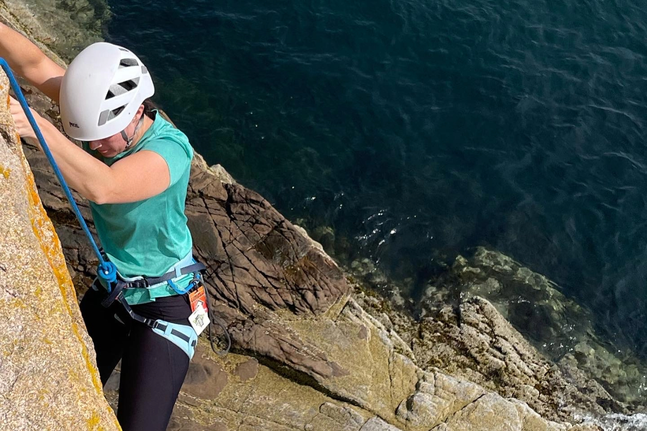一名女子在水上陡峭的悬崖上攀岩