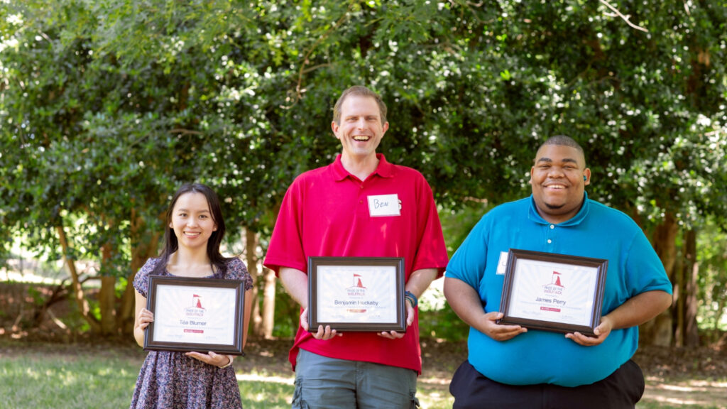 Three people posing outdoors with award certificates