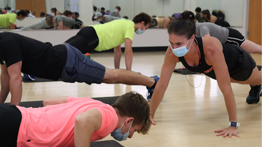 A woman in a mask doing pushups with college students