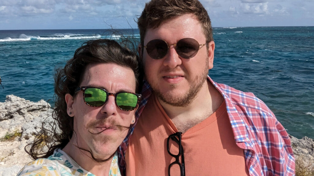 Two men posing in front of a rocky ocean coast