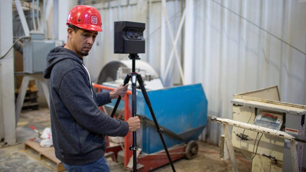 A man in a hardhat adjusting a VR imaging device in a warehouse