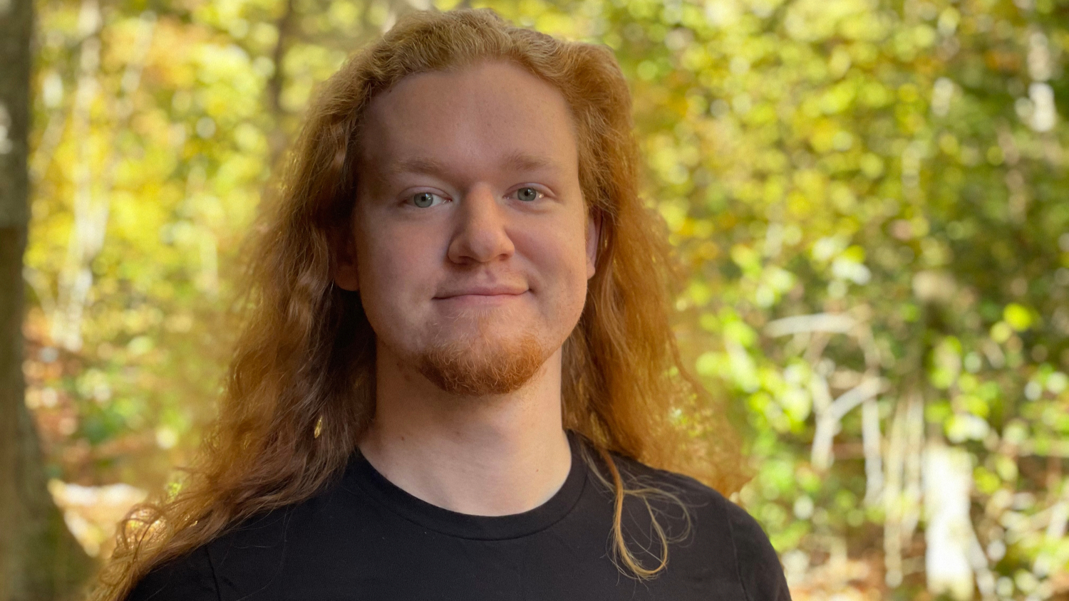 A headshot of a man standing outdoors in green space.