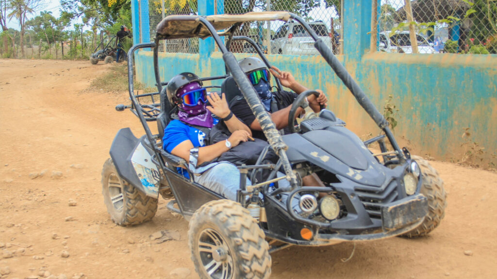 Two people sitting in a dune buggy with bandanas over their faces and google over their eyes.